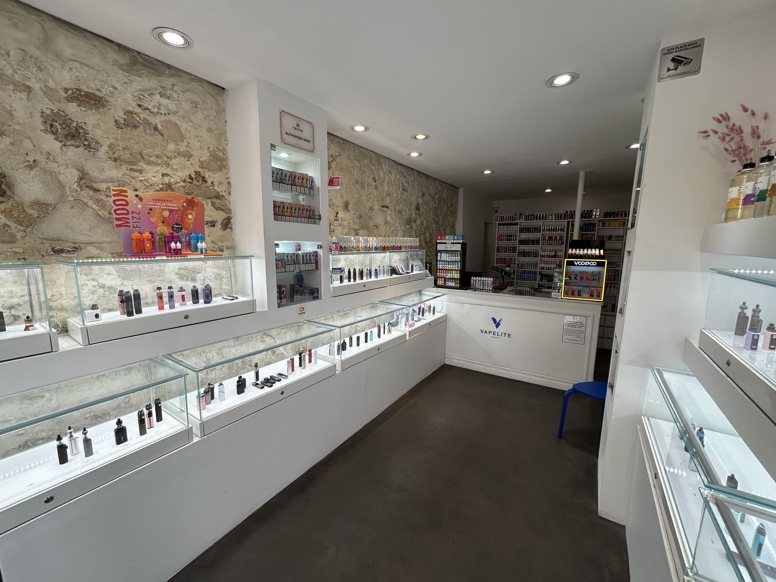 Intérieur de la Maison Vapelite : vitrines lumineuses de cigarettes électroniques, comptoir au logo Vapelite et mur d’e-liquides