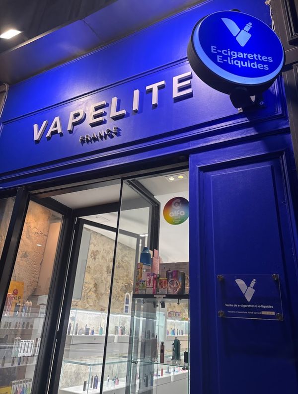 La devanture Vapelite éclairée le soir, avec l’enseigne « E-cigarettes E-liquides »